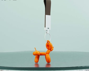 Puede incluir: Un animal de globo naranja con forma de perro cuelga de un llavero marrón y blanco. El llavero está unido a un anillo plateado. El animal de globo está sobre una mesa de vidrio con una superficie moteada blanca y gris.  .STL Descarga digital para impresión 3D