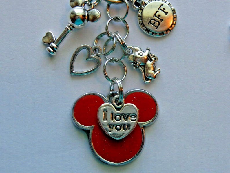 May include: Silver-toned keychain with multiple charms. Charms include a key, heart, mouse, and a round charm with "BFF" engraved. The main charm is a red Mickey Mouse head with a heart that says "I love you".