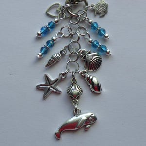 May include: A silver-toned charm bracelet with various ocean-themed pendants. Charms include a starfish, seashells, a manatee, and a fish. Strands of blue beads add color and detail to the design. A heart-shaped charm is also included.