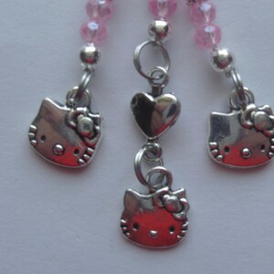 May include: A decorative charm accessory featuring three silver-toned metal Hello Kitty character pendants suspended from silver jump rings. The central charm includes a small silver heart bead, and all three strands are accented with pink beads.