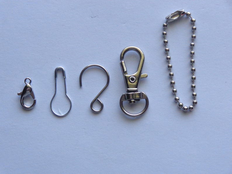 May include: An assortment of silver-colored metal findings, including a lobster clasp, a safety pin style clasp, a curved hook, a swivel clasp, and a ball chain. These findings are commonly used in jewelry making and crafting projects.