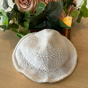 Puede incluir: Sombrero de sol blanco de crochet con un ala ancha y un borde festoneado.