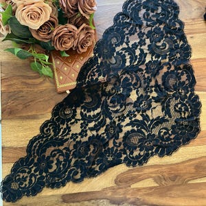 Peut inclure: Un chemin de table en dentelle noire avec un motif floral est présenté sur une surface en bois. Le chemin de table a un bord festonné et se trouve à côté d'un bouquet de roses pêche et marron et d'un petit livre marron.