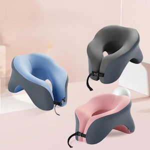 May include: Three travel neck pillows in different colours: blue, grey, and pink. Each pillow has a contoured shape to support the head and neck, and a strap to secure it around the neck.