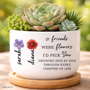 May include: A white ceramic planter with a wooden base, filled with succulents. The planter has the text "If friends were flowers, I'd pick you" and the names "Sarah" and "Diana". The planter is a decorative item.