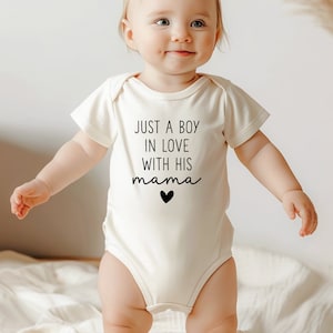 May include: A white baby onesie with short sleeves and the text "JUST A BOY IN LOVE WITH HIS mama" in black with a small black heart.