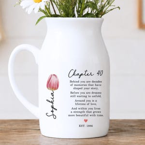 May include: A white ceramic pitcher vase featuring a pink tulip illustration, the name Sophia, and the text Chapter 40, followed by a sentimental poem about memories, love, and strength, ending with a small red heart and the text EST. 1986.