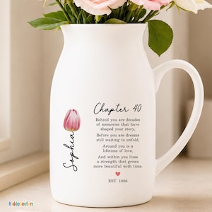 May include: A white ceramic pitcher filled with pink roses. The pitcher features black text that reads Chapter 40, a poem about memories and love, the name Sophia written vertically next to a pink tulip illustration, a small red heart, and EST. 1986.