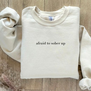 May include: A beige sweatshirt with the text "afraid to sober up" printed on the front.