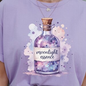 Puede incluir: Camiseta lila claro con una ilustración en acuarela de una botella de vidrio con tapón de corcho. La botella contiene un diseño de galaxia y las palabras "moonlight essence" están impresas en una etiqueta.