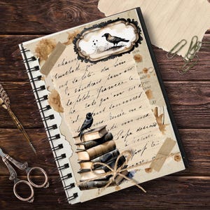 May include: A vintage-style journal with a black and white illustration of a raven perched on a stack of books. The journal has a spiral binding and is decorated with brown paper tape and coffee stains.