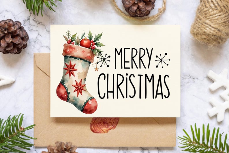 May include: A cream-colored Christmas card with a watercolor illustration of a festive stocking, adorned with red stars and berries. The card reads "MERRY CHRISTMAS" in black lettering. The card is placed on a marble surface with pinecones and greenery.