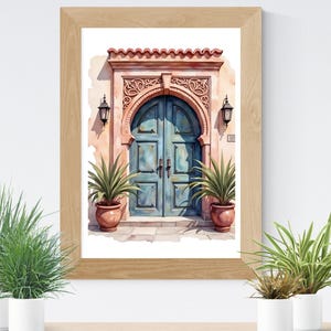 May include: Watercolor painting of a teal arched door with a detailed stone frame, flanked by two lanterns. The door is set in a peach-colored wall, and the artwork is framed in a light wood frame. Potted plants are in front of the artwork.
