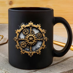 May include: Black ceramic mug featuring a steampunk-style gear design in gold and bronze tones. The gear design is centered on the mug, with intricate details. The mug has a curved handle and is set against a neutral background.