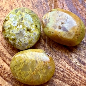 May include: Three smooth, polished green and yellow opal stones. The stones are oval shaped and have a natural, organic look.