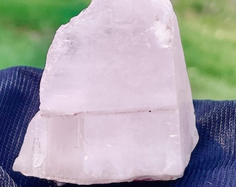 May include: A large, pale pink, translucent crystal with a smooth, flat surface. The crystal has a slight, natural, pink hue and is shaped like a pyramid.