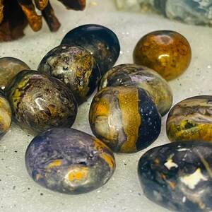 May include: A collection of tumbled stones with a variety of brown, black, and white patterns. The stones are smooth and polished, and they have a natural, organic look.
