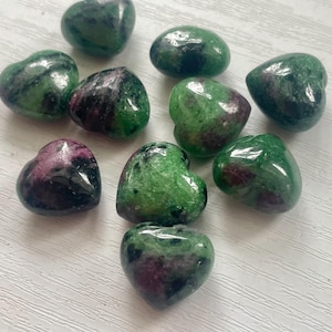 May include: A collection of ten green and black heart-shaped gemstones. The stones have a mottled appearance with shades of green and black.