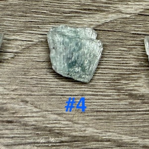 May include: Three light blue, raw mineral specimens with a crystalline structure are displayed on a wooden surface. Each piece is labeled with a blue number: #3, #4, and #5. The minerals have a textured, layered appearance.