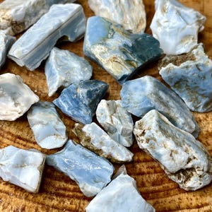 May include: A collection of blue and white opal rough stones. The stones are various shapes and sizes and have a natural, raw look.