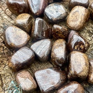 Puede incluir: Una colección de piedras de spectrolite marrones y plateadas pulidas. Las piedras son lisas y pulidas, con una variedad de formas y tamaños.