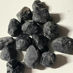 May include: A collection of black obsidian tumbled stones. The stones are smooth and polished, with a variety of shapes and sizes.