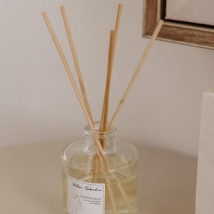 Puede incluir: Una botella de vidrio transparente con una etiqueta que dice "Kristian Babardino EGYPTIAN NIGHT Interior oil reed diffuser Home fragrance" y un diseño de rostro de mujer. La botella está llena de un líquido transparente y tiene palitos de madera insertados.