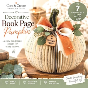 May include: A decorative pumpkin crafted from folded book pages, featuring a dark green velvet stem, a burnt orange and cream frayed ribbon bow, and a small wooden tag engraved with the word Grateful. The pumpkin is adorned with green leaves.
