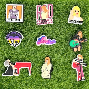 May include: Nine colorful shoe charms featuring Taylor Swift album covers and lyrics. The charms include a photo of Taylor Swift, the words "Red Taylor's Version", "Lover", "Taylor Swift", "Peter Losing Wendy", and a piano with a person sitting at it.