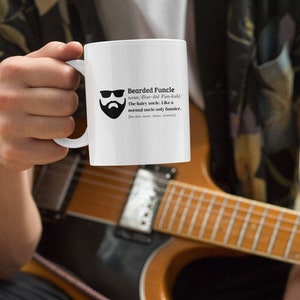 May include: White ceramic mug with the text "Bearded Funcle" and a graphic of a bearded face wearing sunglasses. The mug also includes a definition of "Funcle". The mug is held in front of a guitar.