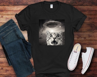 May include: A black t-shirt with a graphic of a cat looking up in surprise at a flying saucer. The cat is in black and white, and the saucer is a light gray.