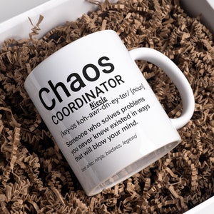 May include: White ceramic mug with black text that reads "Chaos Coordinator" and a definition of the word. The mug is sitting in a white box filled with brown packing paper.