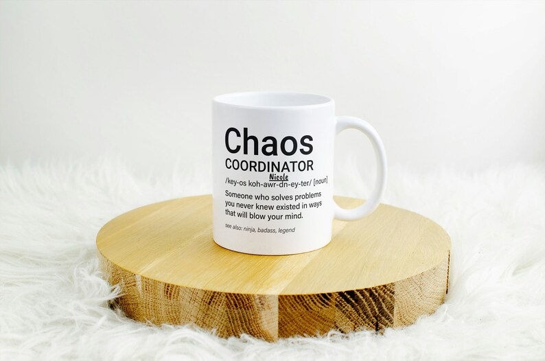 May include: White ceramic mug with a black graphic that reads "Chaos Coordinator" and a definition of the word. The mug is sitting on a wooden coaster.