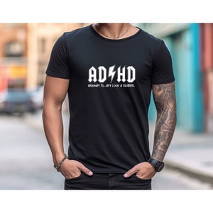 Może przedstawiać: Czarny T-shirt z białym nadrukiem, na którym widnieje napis "ADHD - HIGHWAY TO...HEY LOOK A SQUIRREL"