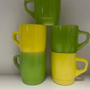 Puede incluir: Conjunto de cuatro tazas vintage, dos verdes y dos amarillas, con un diseño texturizado alrededor de la base. Las tazas están apiladas en forma de pirámide.