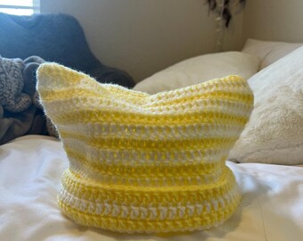 May include: A yellow and white striped crocheted hat. The hat is made with a simple stitch and has a wide brim.