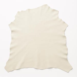 May include: A piece of ivory-colored leather with a smooth surface and irregular edges. The leather is a single, large piece, likely for crafting or upholstery projects. The neutral color and natural shape suggest a focus on quality materials.