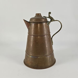 May include: A vintage copper teapot with a brass lid and handle. The teapot has a rounded body and a spout on the side.