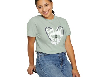 May include: A woman wearing a light green t-shirt with a white graphic that says "Pickleball & Jesus" in a heart shape. The graphic is in a retro font style.