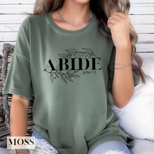 May include: A green t-shirt with the word "ABIDE" in black lettering surrounded by a floral design. The text "John 15" is written below the word "ABIDE".