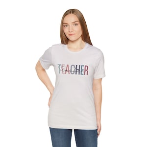 May include: White t-shirt with a colorful graphic that says "Teacher" in a stylized font.