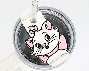 May include: White tumbler with a clear straw and a decorative charm featuring a cartoon cat with a pink bow. The cat charm is white with pink accents and black details. The tumbler has a white handle.
