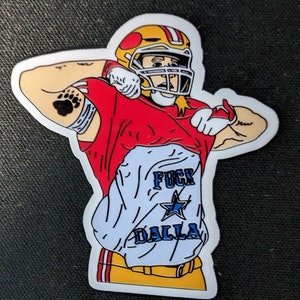 May include: A die-cut sticker featuring a football player in a red and gold uniform with a helmet, lifting their jersey to reveal a white undershirt with the text FUCK DALLA and a blue star graphic. The player has a bear paw tattoo on their arm.