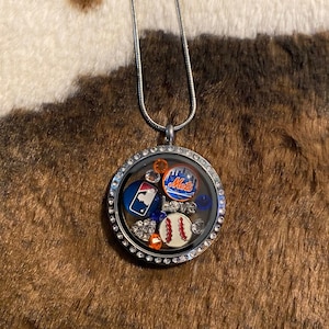 May include: A silver chain necklace with a round locket featuring a baseball theme. The locket has a clear glass front and is filled with various baseball-themed charms, including a baseball, a baseball bat, and a New York Mets logo. The locket is surrounded by a row of clear rhinestones.