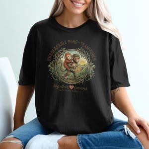May include: Black t-shirt featuring a circular graphic of two monkeys in a forest setting. The graphic includes the text "UNBREAKABLE BOND - TEAM PUNCH" and "together forever". The shirt is worn by a person.