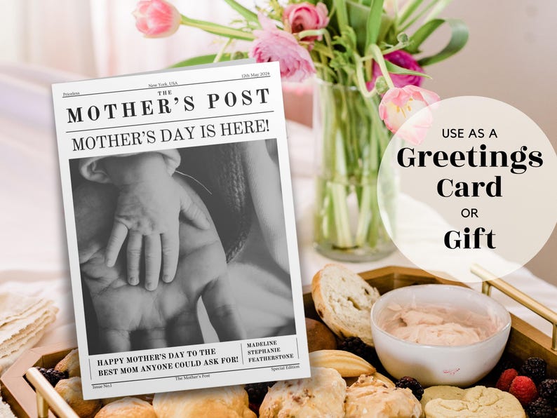 May include: A black and white newspaper-style card with the text "The Mother's Post" and "Mother's Day is Here!"  The card features a photo of hands, one adult and one child, with the text "Happy Mother's Day to the Best Mom Anyone Could Ask For!"  The card is on a table with a plate of food and a vase of pink flowers.
