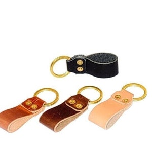 May include: Four leather keychains with brass rings and gold-toned rivets. The keychains are in black, brown, tan, and natural leather.