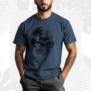 K&ouml;nnte beinhalten: Ein marineblaues T-Shirt mit einer schwarzen Grafik eines Sch&auml;dels an einem Strand mit Palmen und V&ouml;geln. Der Text "NOMAD TREK" ist darunter aufgedruckt, zusammen mit den S&auml;tzen "NO MAP - NO MASTER" und "EST 2020".