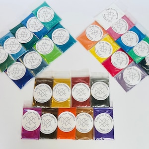 May include: Assortment of 24 small bags of High Line Pigments, each containing a different color powder pigment. The bags are arranged in rows on a white surface. The colors include: Aquamarine, Pelagic Green, Sea Turtle, Mustique, Galactic Violet, Shadow Run, Magic Koi Green, Peacock Blue, Bronze, Gold, Ruby, Sterling Grey, Tourmaline, Brown, Fire Opal, Copper, Amethyst, White Pearl, Pink, Blue, Green, Black, Red, Violet, Orange, Yellow.