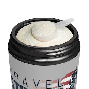 Puede incluir: Primer plano de un recipiente negro y gris lleno de un polvo de color claro, con una cuchara blanca encima. El recipiente tiene las palabras "GRAVEL STIR" impresas, junto con un gráfico de ciclista y una bandera americana.